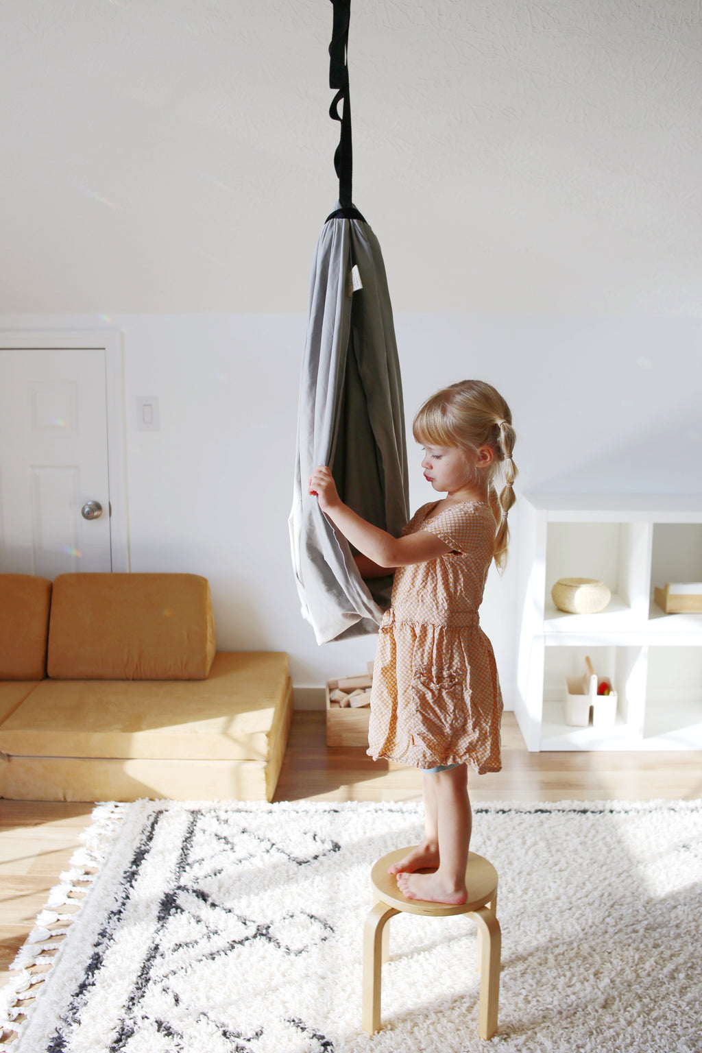 Child preparing to climb into a Stone double-layer sensory swing in an indoor playroom.