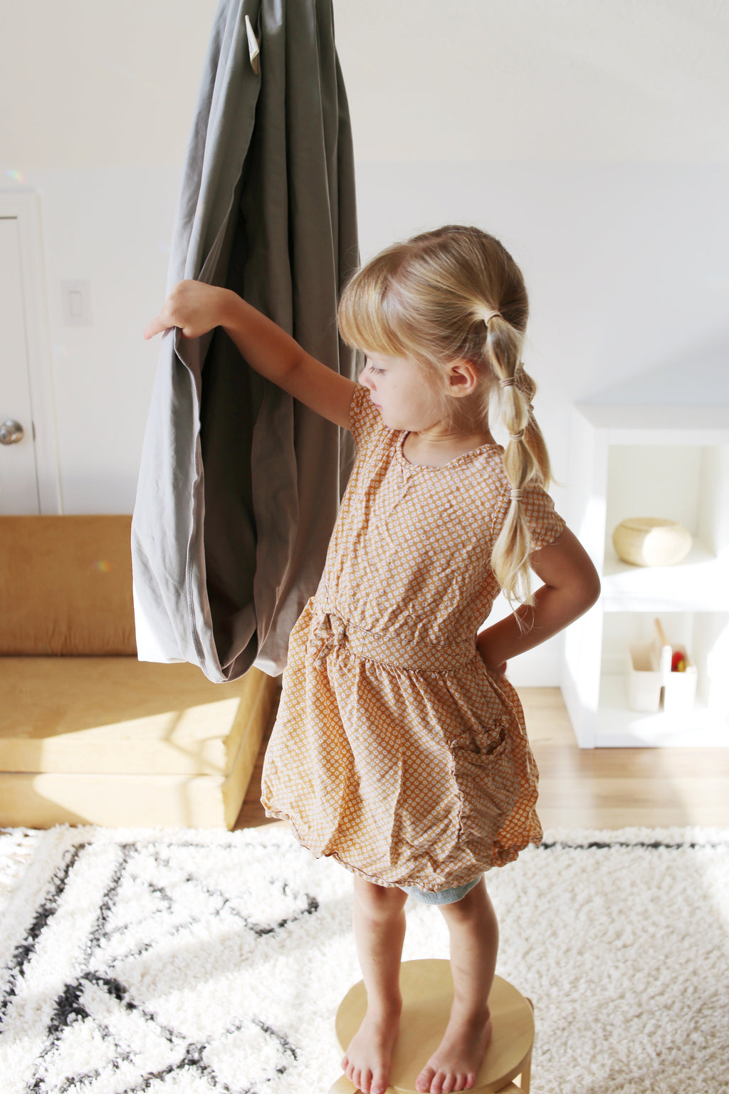 Child standing beside a Stone double-layer sensory swing hanging in an indoor playroom.