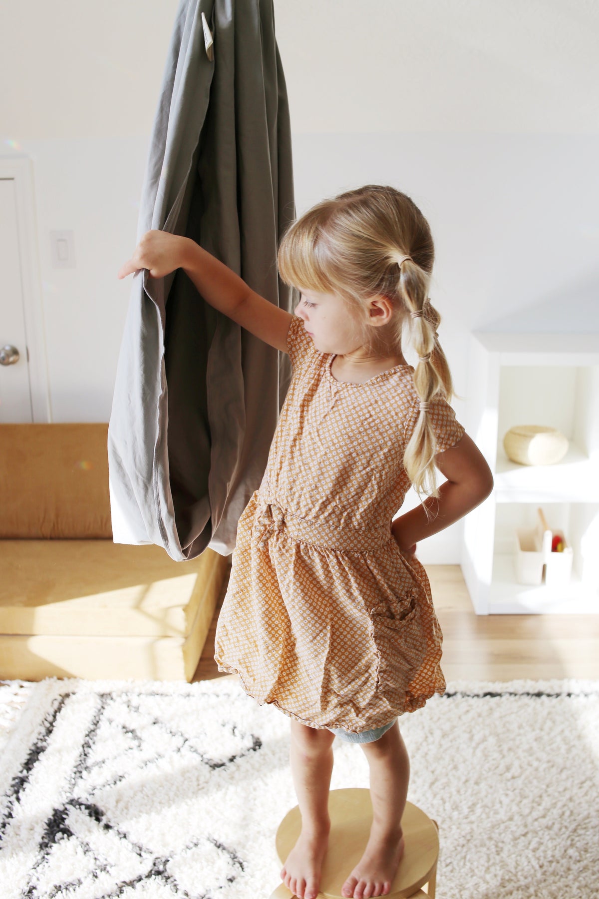 Child standing beside a Stone double-layer sensory swing hanging in an indoor playroom.