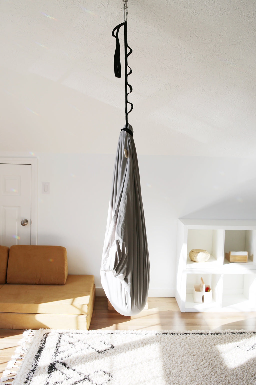 Stone double-layer sensory swing hanging from an adjustable daisy chain strap in an indoor playroom.