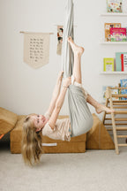 Child swinging playfully in a Stone double-layer sensory swing in an indoor playroom.