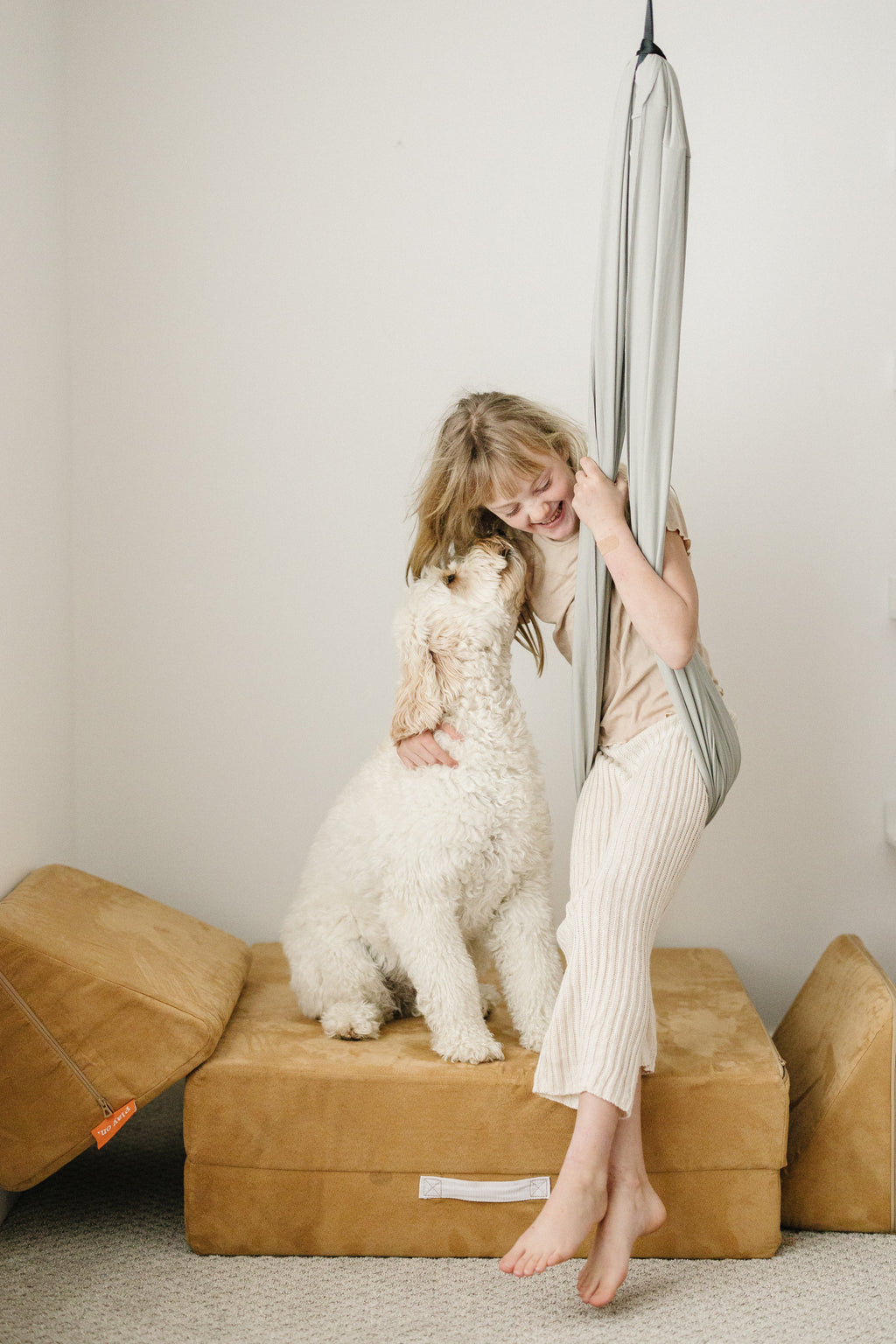 Child relaxing in a Stone double-layer sensory swing with a dog beside her in a playroom.