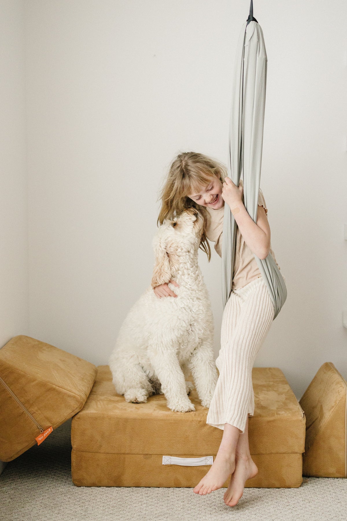 Child relaxing in a Stone double-layer sensory swing with a dog beside her in a playroom.