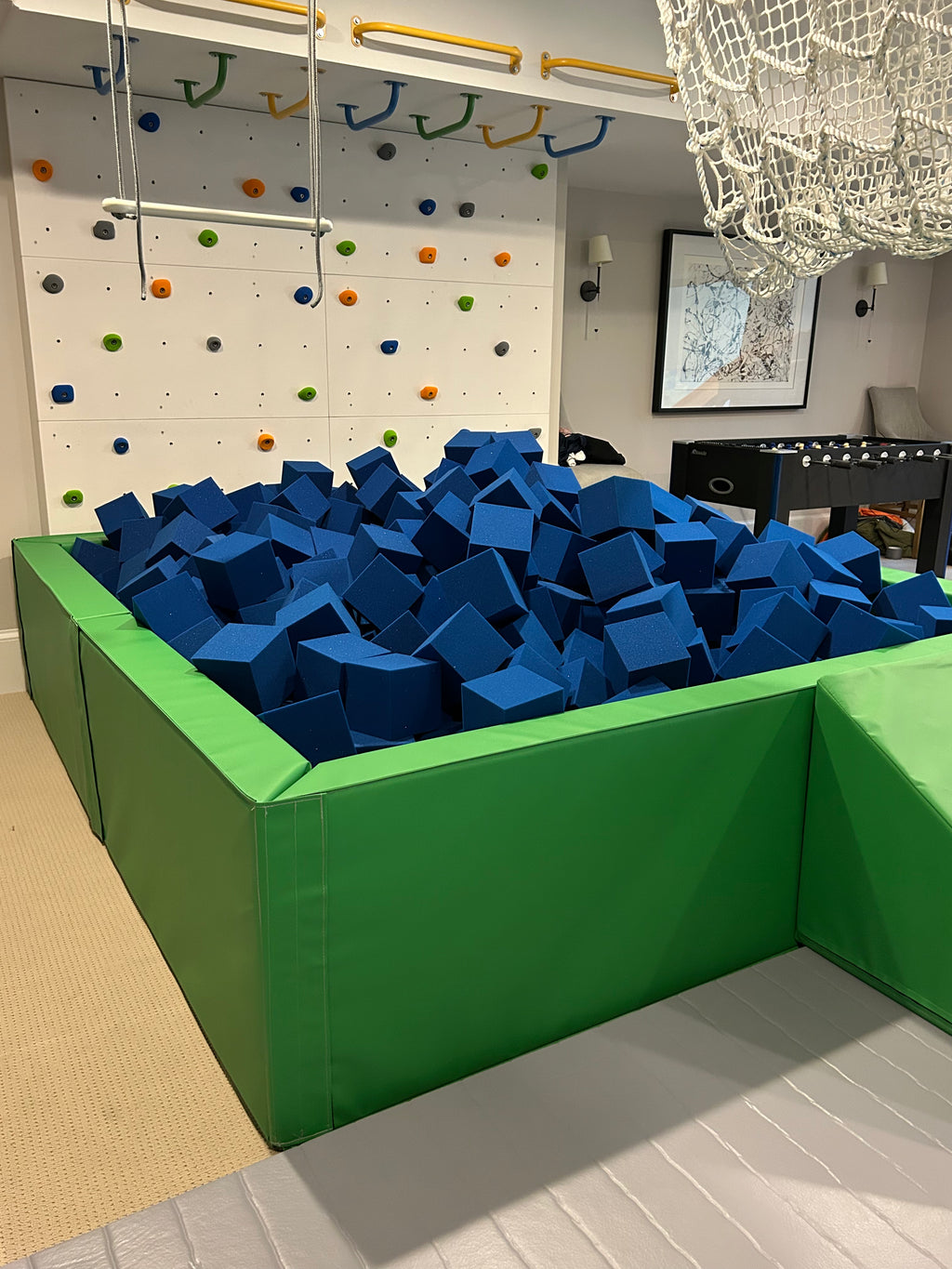 Blue foam cubes in a green foam pit beside a climbing wall