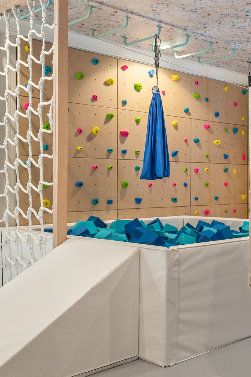 Blue sensory swing hanging over foam pit in front of colorful climbing wall
