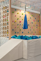 Blue sensory swing hanging over foam pit in front of colorful climbing wall