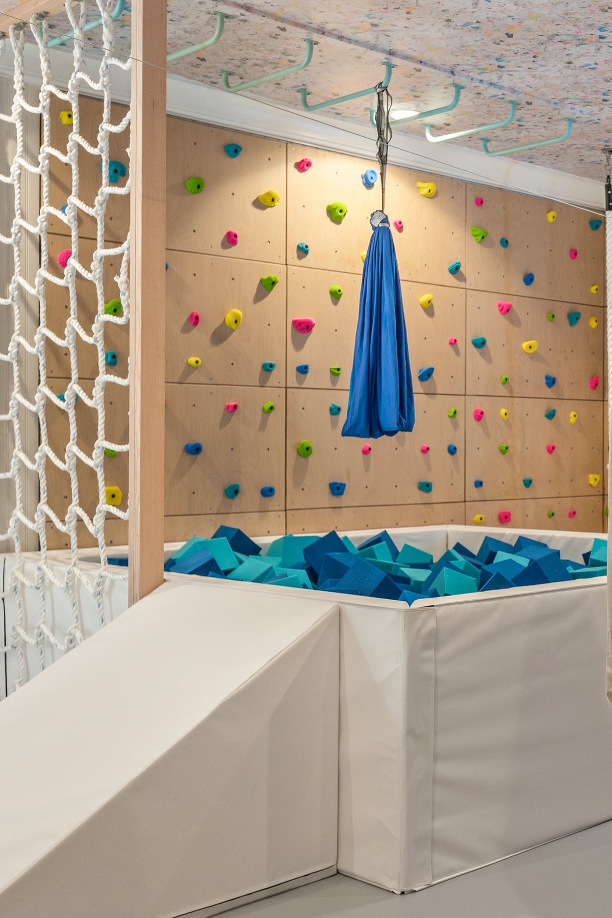 Blue sensory swing hanging over foam pit in front of colorful climbing wall