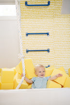 Toddler holding  a climbing  rope in a foam pit filled with yellow foam cubes