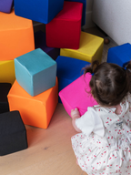 Toddler playing in a pile of foam cubes with washable fabric covers in orange, pink, blue, turquoise and red