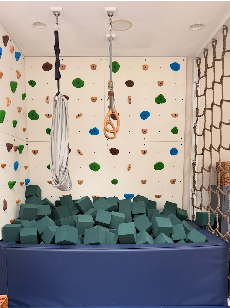 Kids indoor playroom with climbing wall, hanging rings and foam pit filled with forest green foam cubes