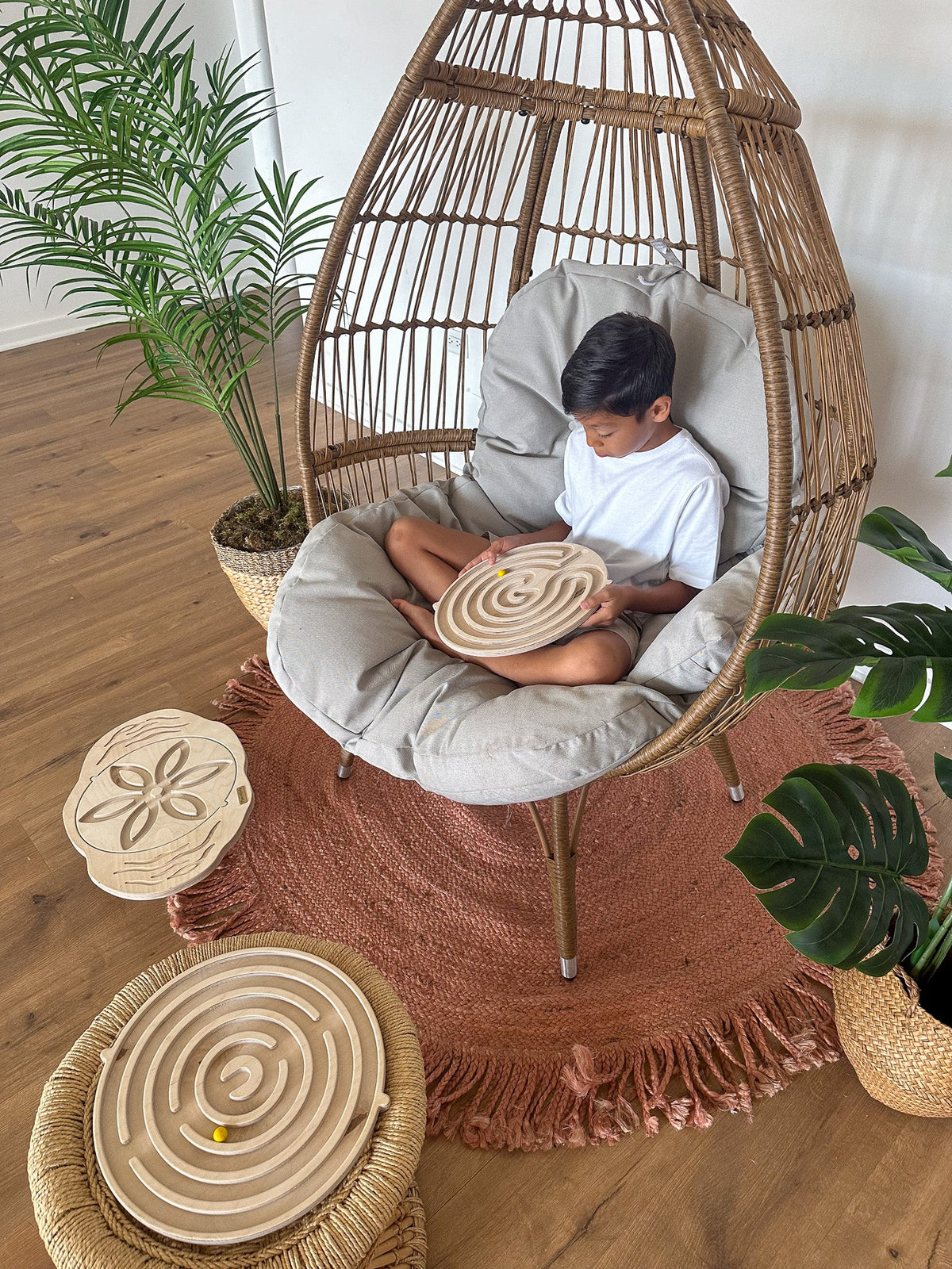 Child in chair playing with wooden maze balance board. swappable boards pictured