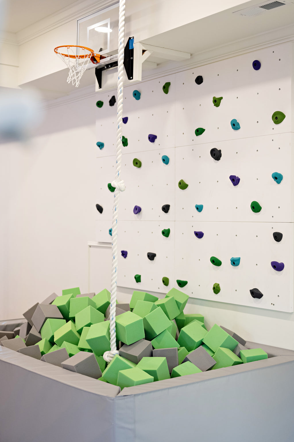 Lime Green and light gray foam cubes in a gray foam pit below a climbing wall and basketball hoop
