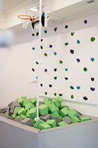 Lime Green and light gray foam cubes in a gray foam pit below a climbing wall and basketball hoop