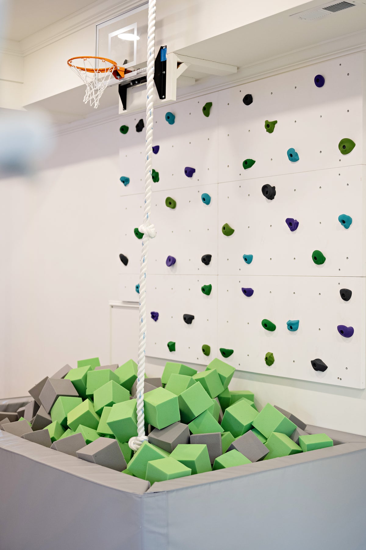 Lime Green and light gray foam cubes in a gray foam pit below a climbing wall and basketball hoop