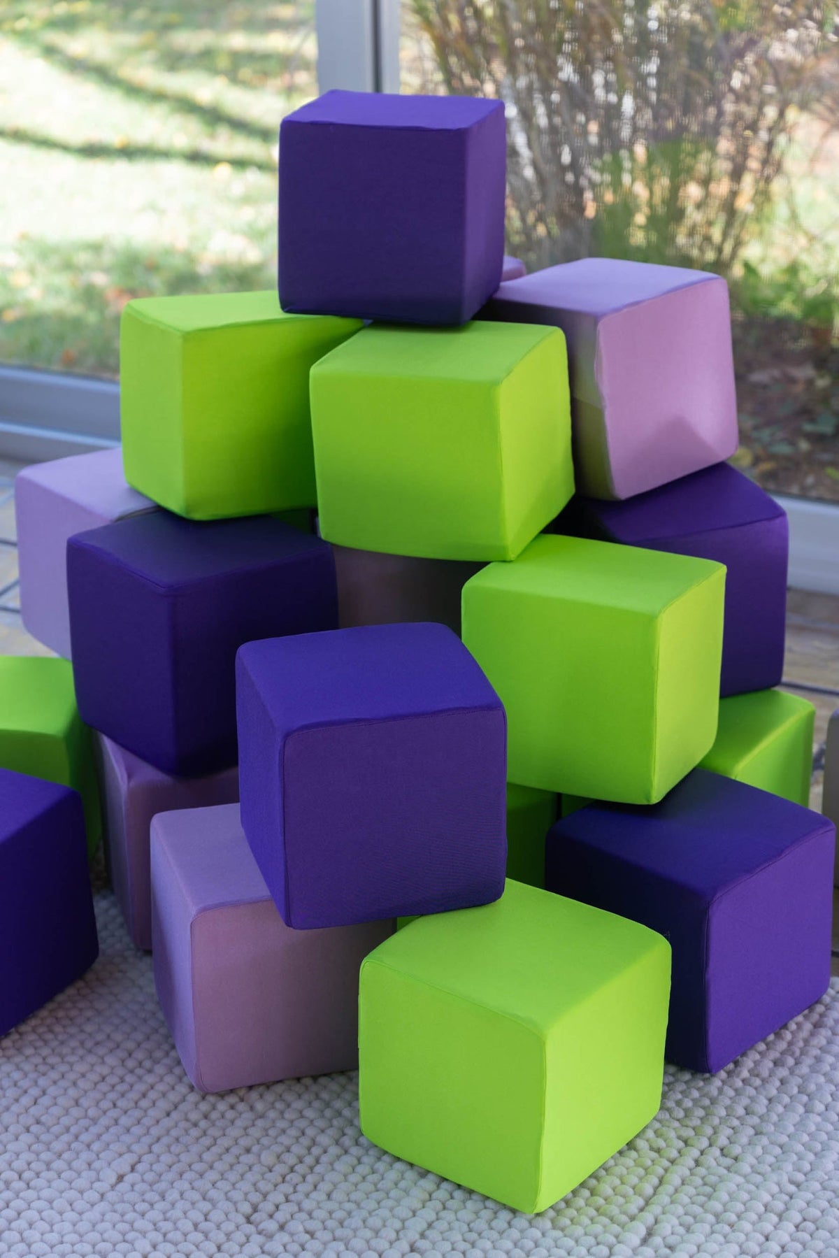 Foam cubes in purple, lavender and lime green covers stacked in a playroom by a window
