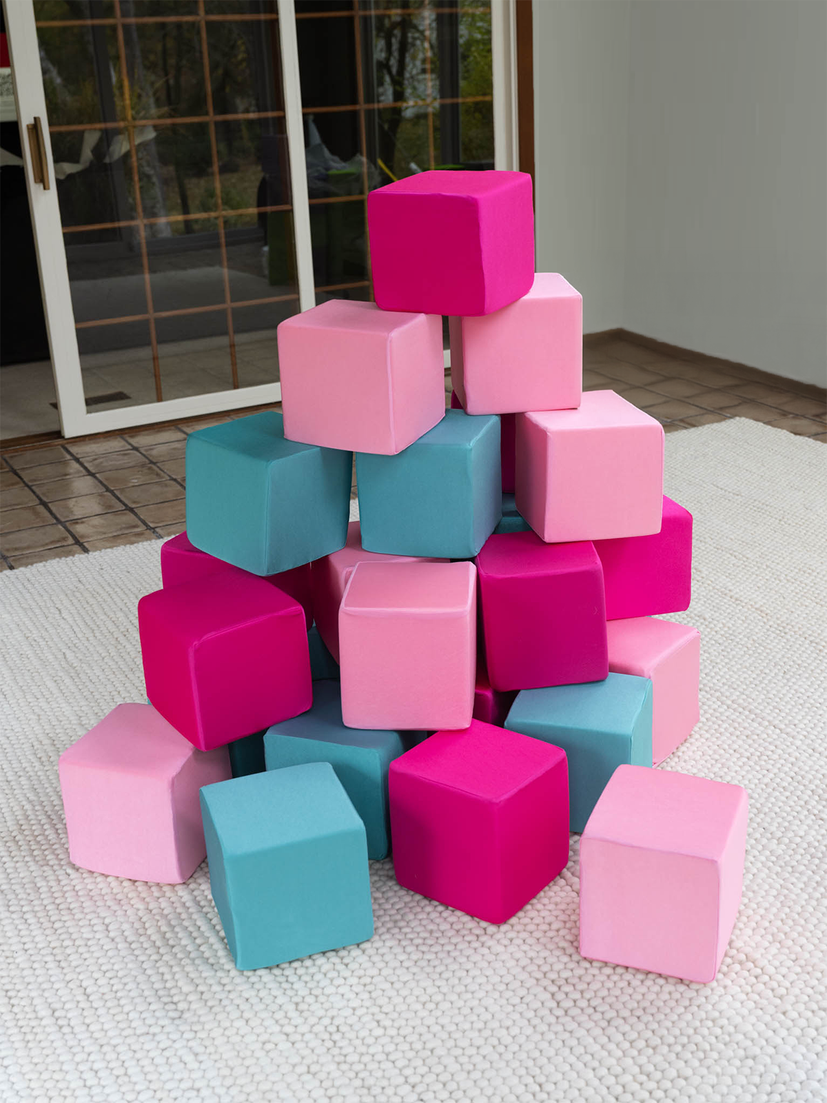 Pyramid of foam cubes in light pink, magenta and turquoise covers on a white playroom rug