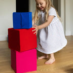 Young girl stacking foam cubes in red, pink and blue covers on a wood floor