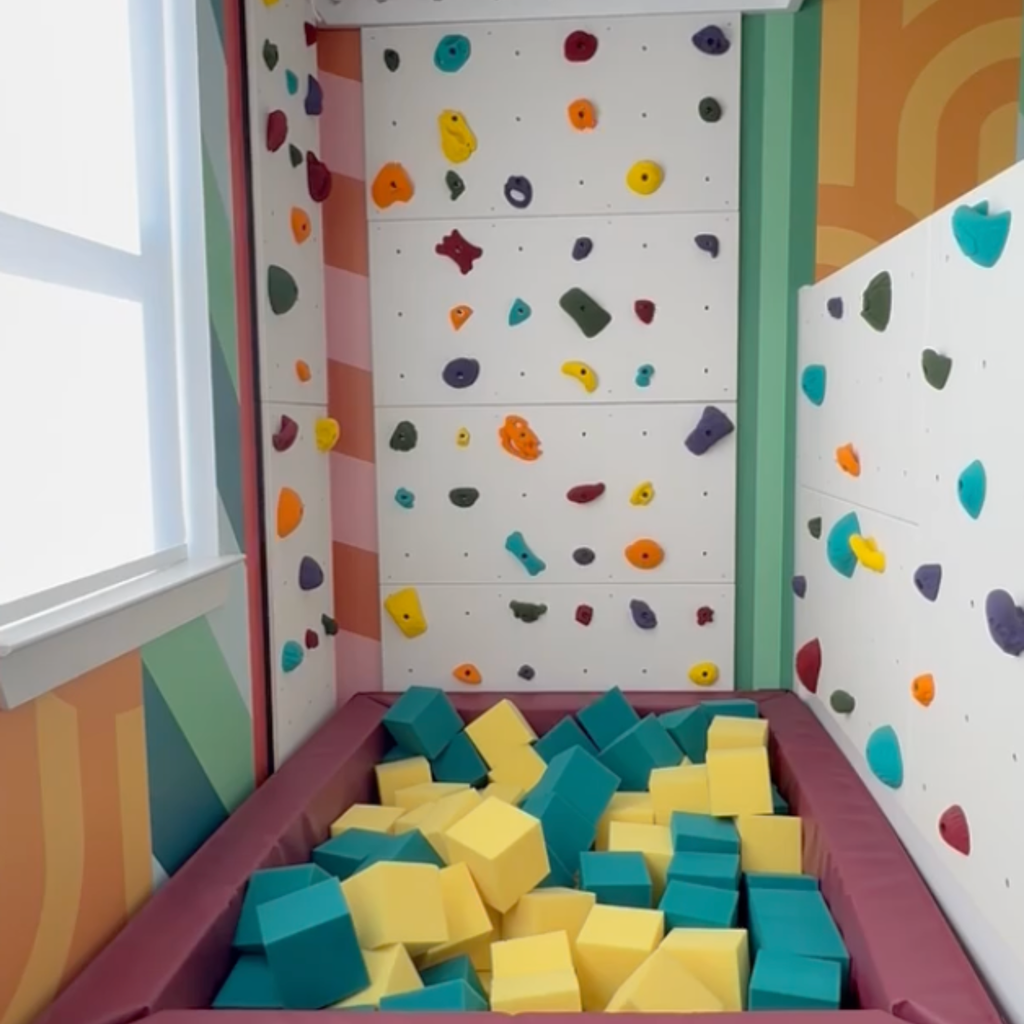 Colorful indoor climbing walls surrounding a foam pit filled with teal and yellow foam cubes