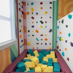 Colorful indoor climbing walls surrounding a foam pit filled with teal and yellow foam cubes