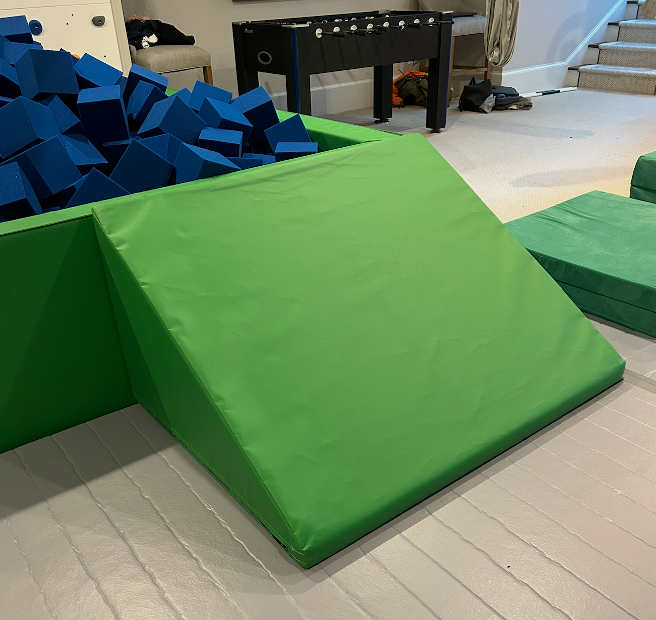 Green foam mats on a wooden floor with blue foam blocks in the background.