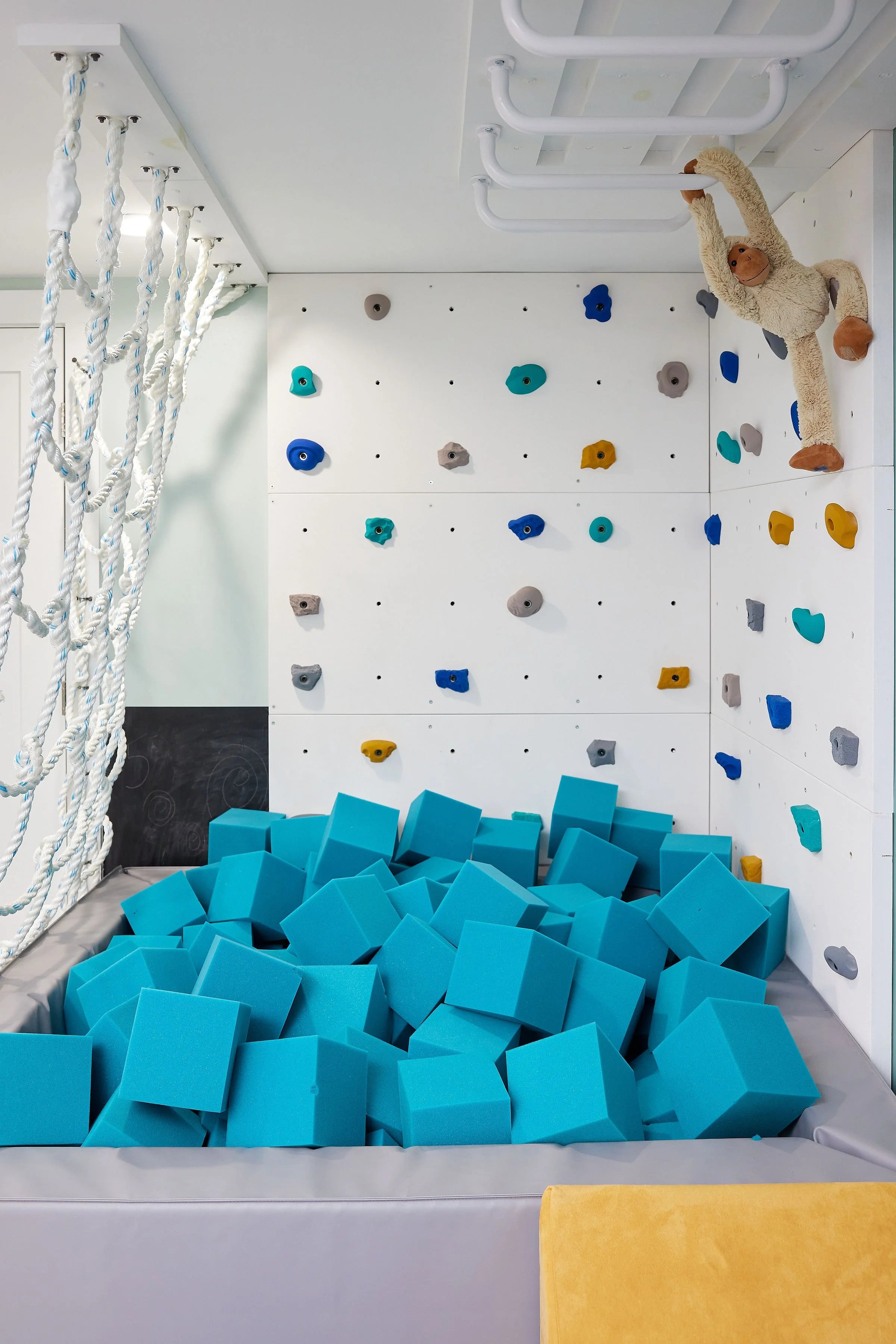 Children's play area with blue foam cubes, climbing wall, and monkey plush toy.