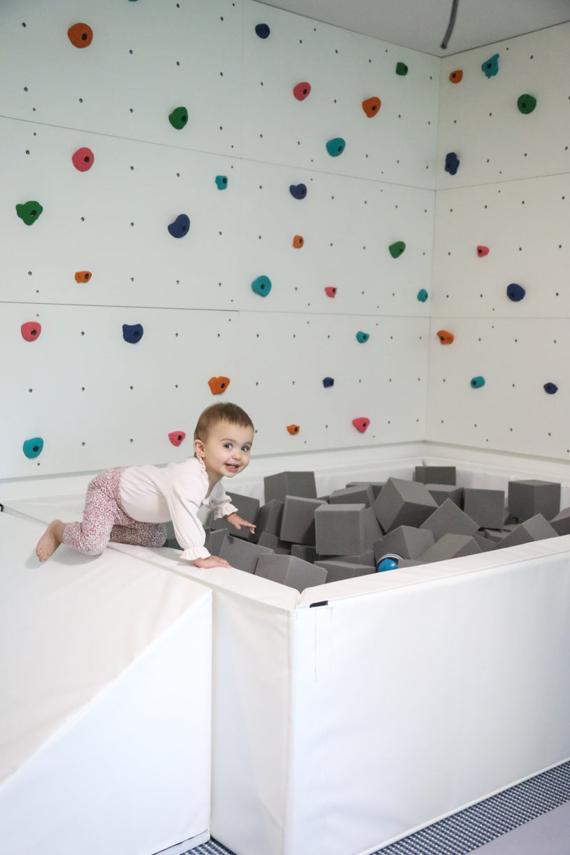 Young child climbing into a white foam pit filled with light gray foam cubes