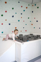 Young child climbing into a white foam pit filled with light gray foam cubes